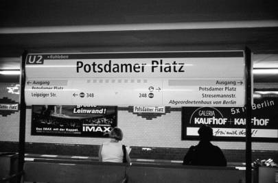 Informationstafel im U-Bahnhof Potsdamer Platz, darunter zwei sitzende Menschen